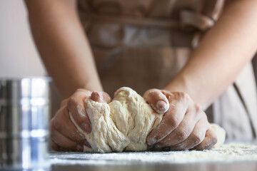 Female chef preparing dough on kitchen table, closeup