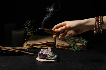 Hand with Palo Santo, minerals and incense on dark background
