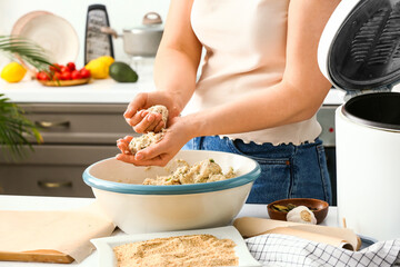 Woman cooking cod cutlets at table in kitchen