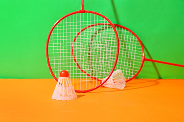 Badminton rackets and shuttlecocks on color background
