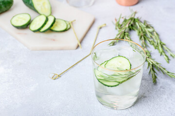 Glass of cold gin tonic and cucumber slices on light background