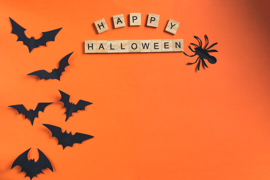 The inscription Happy Halloween made from wooden cubes and bats cut from black paper on an orange background. All saints day concept and paper decorations. Paper cut style.Flatlay, Copy Space