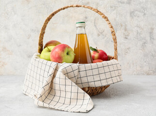 Basket with bottle of apple juice and fresh fruits on light background