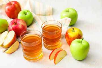 Glasses of apple juice and fresh fruits on light background