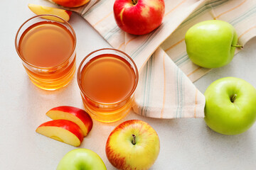 Glasses of apple juice and fresh fruits on light background