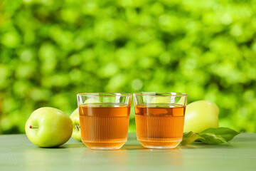 Glasses of apple juice and fresh fruits on table outdoors