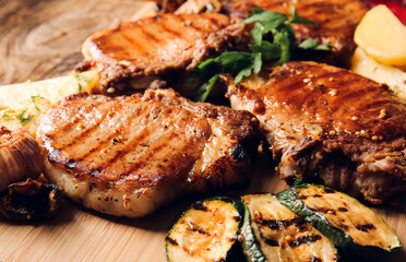 Board with tasty pork steaks and grilled vegetables on wooden background