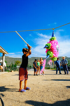 Boy swinging stick to hit pinata while family celebrating Mexican culture at backyard on sunny day