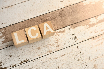 On a white damaged wood board, wooden word cubes are arranged in the letters LCA. It is an...