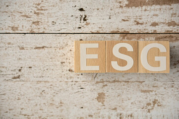 On a white damaged wood board, wooden word cubes are arranged in the letters ESG. It is an abbreviation for Environment, Social, Governance.