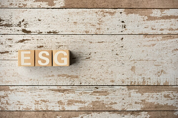 On a white damaged wood board, wooden word cubes are arranged in the letters ESG. It is an abbreviation for Environment, Social, Governance.