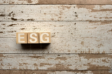 On a white damaged wood board, wooden word cubes are arranged in the letters ESG. It is an abbreviation for Environment, Social, Governance.