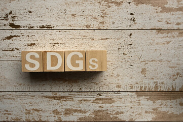 On a white damaged wood board, wooden word cubes are arranged in the letters SDGs. It is an abbreviation for Sustainable Development Goals.