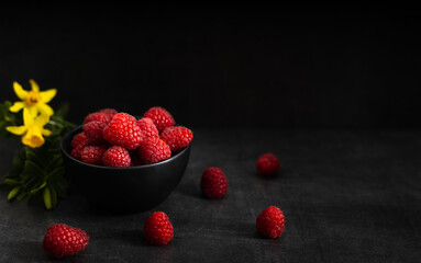 red raspberry in a black bowl on a dark background. Fruit, red raspberry in a black bowl on a dark background with a bottle of juice on the side.