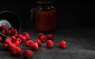 red raspberry in a black bowl on a dark background. Fruit, red raspberry in a black bowl on a dark background with a bottle of juice on the side.