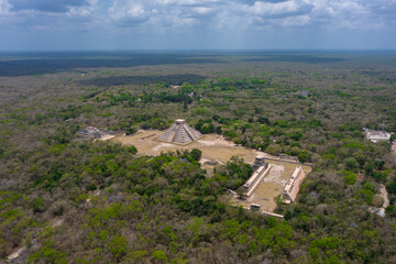 Aerial view of the beautiful Chicen Itza and Mayan Pyramid in Mexico surrounded with ground and greenery with ocean under cloudy sky during day