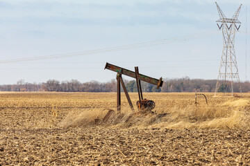 Old, orphaned oil well pump in farm field.  oil well abandonment, decommission, and oil production concept. - obrazy, fototapety, plakaty