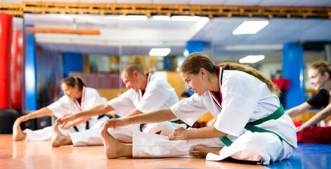People in kimono warming up before karate training. They're doing stretching exercises for legs. © JackF