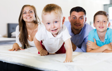 Little smiling boy with brother and parents testing mattress in store