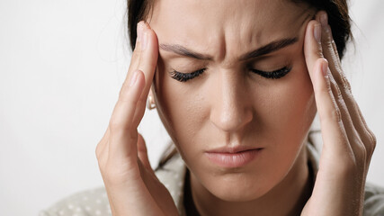 Fototapeta premium Headache. Suffering woman on white background holds her head with her hands. Stress, fatigue, migraine, high or low blood pressure concept