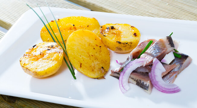 Delicious slices of pickled herring with pieces of roasted potatoes and herbs