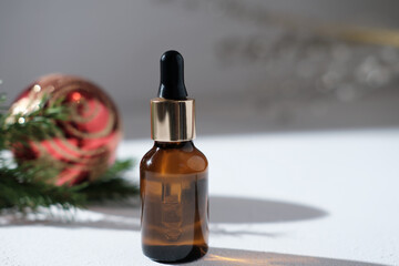 face care serum or oil in amber glass bottle with dropper next to christmas decor on a table. red christmas ball and pine branch. copy space. cosmetic seasonal sale.