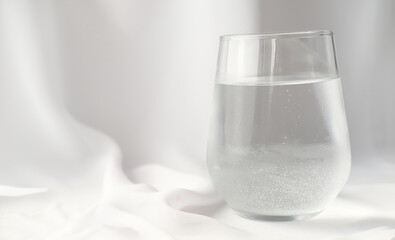 a glass of sparkling mineral water white silk background. water drinking, morning rituals, trendy styled composition