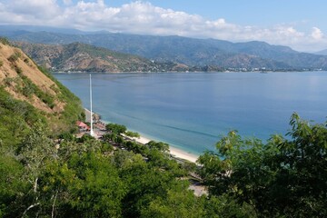 Fototapeta premium A view of white sandy beach, turquoise sea and surrounding hills of capital Dili, Timor Leste
