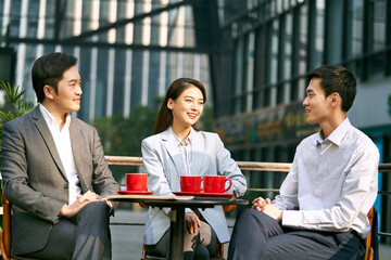 team of three happy asian business people meeting chatting relaxing in outdoor cafe