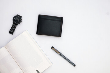 Fashionable black leather men's wallet with watch, blank book and pen on white office desk, white table. Work desk  view. Top angle work desk. Flat lay work desk