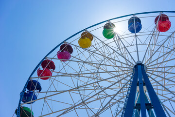 Ferris wheel with colored cabins on background of blue sky