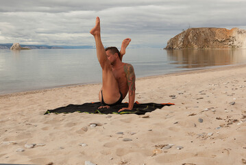 strong young man does yoga on the sandy shore of a mountain lake, yoga practice on the beach