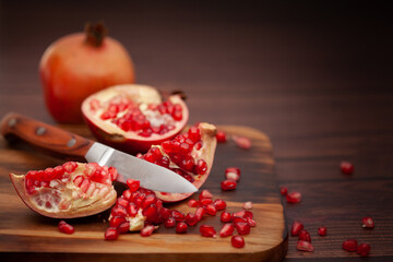 Close-up of organic red pomegranate seed (Punica granatum) on wooden board with knife  over wooden background.
