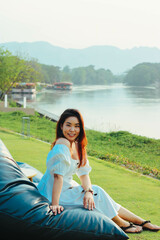 Beautiful Asian woman relaxing on blue bean bag chair on the grass near river