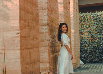 Asian woman wears white dress smiling to camera with wooden wall background in hotel