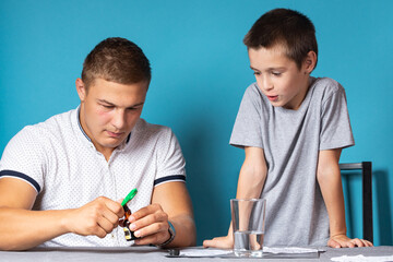 Dad and son are conducting chemical experiments, observing the change in color of a chameleon as a...