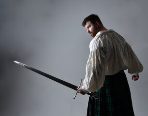 Close up portrait of handsome brunette man wearing Scottish kilt and renaissance white  pirate...