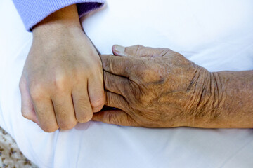 Close up photo of child hand holding her elderly grandmother laying in bed