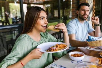 young latin woman eating mexican tacos on a restaurant terrace in Mexico Latin America, feeling happy on a summer day