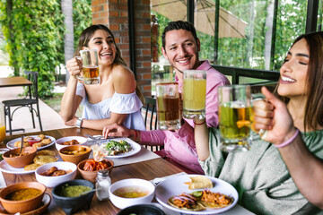 Group of Young latin Friends Meeting For beer, michelada Drinks And mexican Food Making A Toast In Restaurant terrace in Mexico Latin America