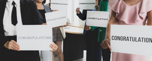 Businesspeople group in business clothes  holding paper banner with word congratulations and show to camera. Concept of greeting and appreciation for success in job or work in company