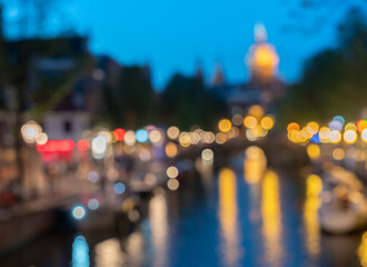 Amsterdam urban night and travel abstract backgrounds defocused lights and buildings along canal with Saint Nicholas Basilica church tower against blue sky.