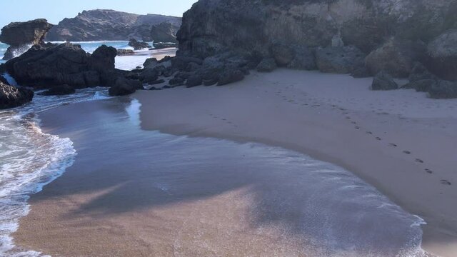 Drone flying low across shoreline passing rocky enclave