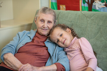 Portrait of an old woman and a little girl, grandmother hugs her granddaughter, family ties, old...