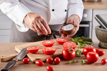 Crop cook pouring salt on fresh tomatoes