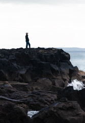 Obraz premium Man standing on rocks looking at the sea. Waves crashing onto the rocks, Takapuna and Milford walkway. Vertical format.