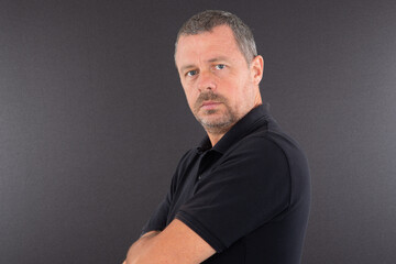 Man in black t-shirt with arms crossed on grey background