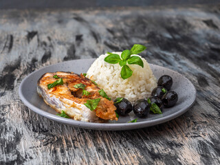 Lunch with rice and fish, olives and green basil, served on a gray plate