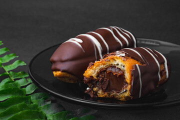 Chocolate bomb. Traditional Brazilian eclair bitten with apparent filling on a black background and branch of leaves. 