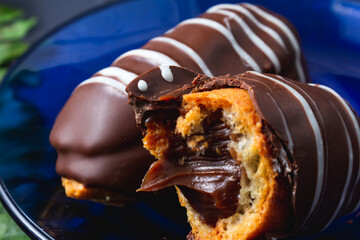 Chocolate bomb. Traditional Brazilian eclair bitten with apparent filling on a black background and branch of leaves. 